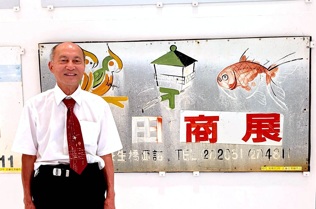 松田保夫社長と、あえて『松田商展』と表記された初代看板