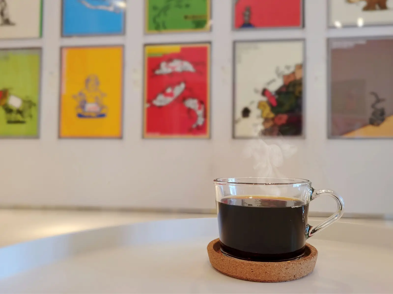 湯気の立つホットコーヒーと、奥にポスター展示が並ぶAPM館内
